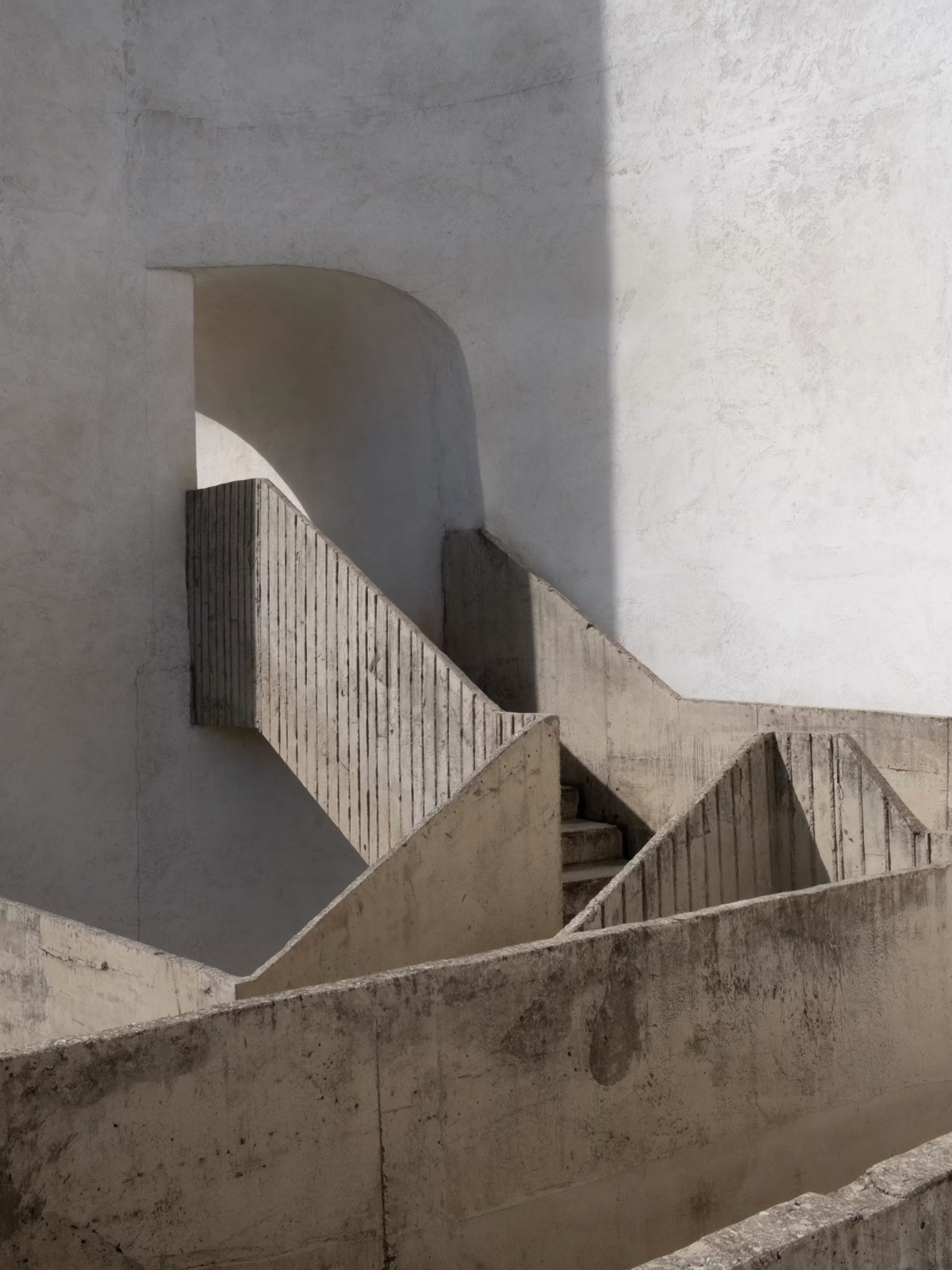 Board-marked concrete stairs turning between white walls