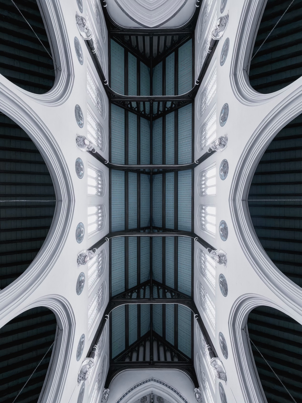 Looking up into a white vaulted ceiling, dark timber between its arches